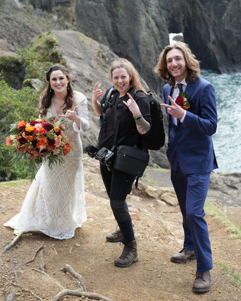 two women and a man standing on a cliff near the ocean