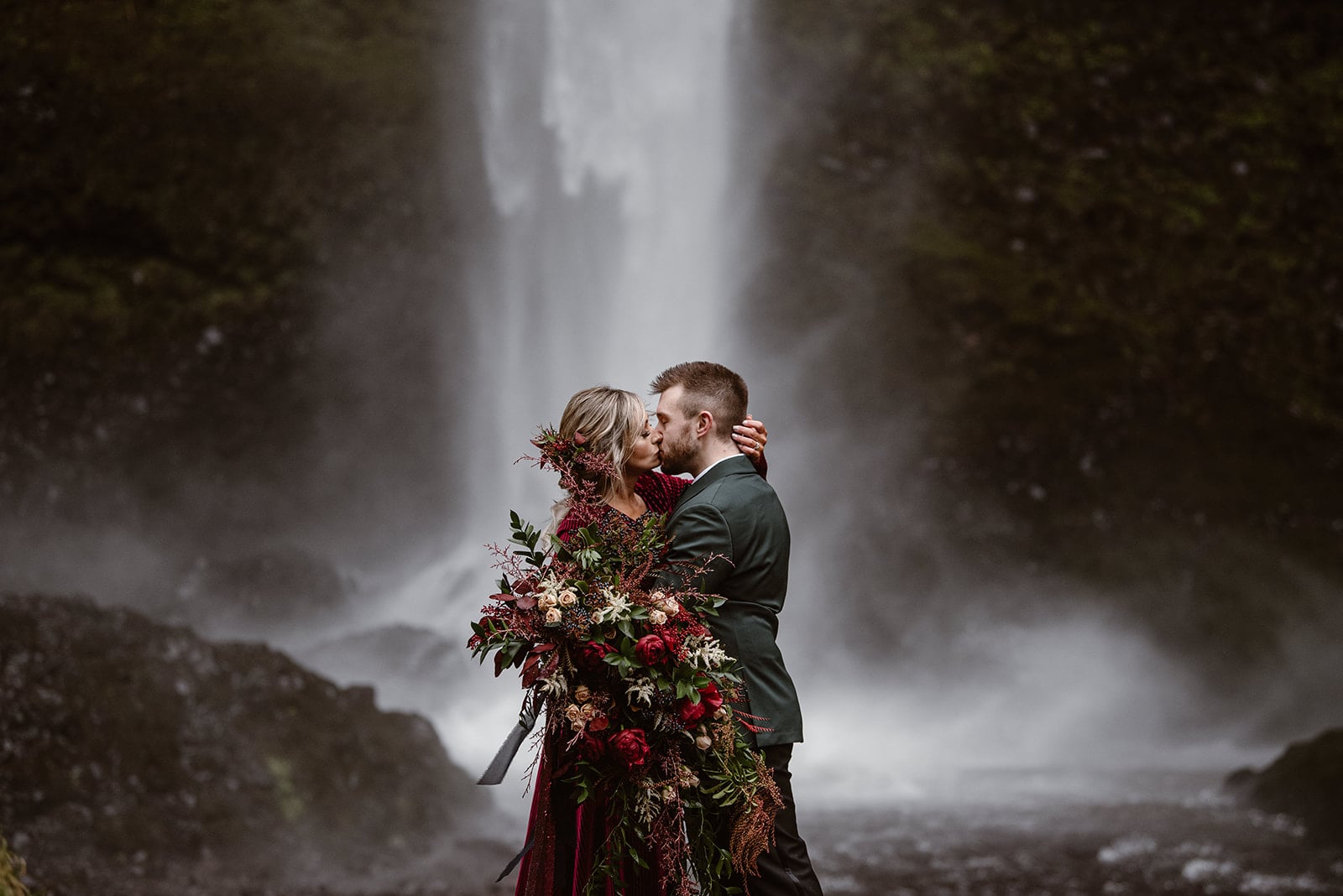 a couple kissing in front of a waterfall