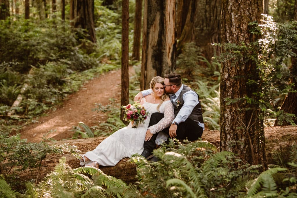 a bride and groom sitting on a log in the woods