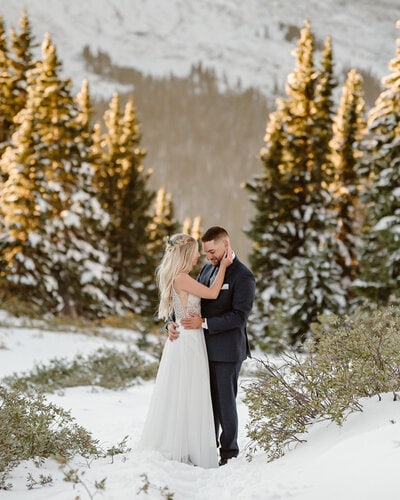 a bride and groom kissing in the snow