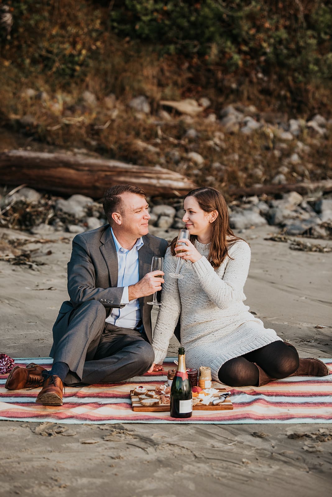 a man and woman sitting on the beach drinking wine