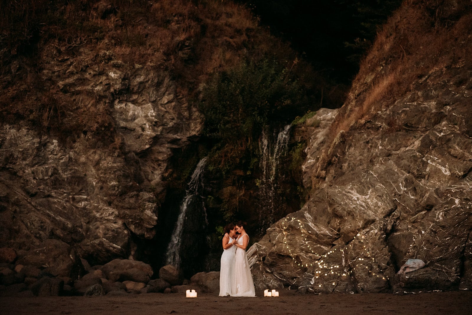 a bride and groom standing in front of a waterfall
