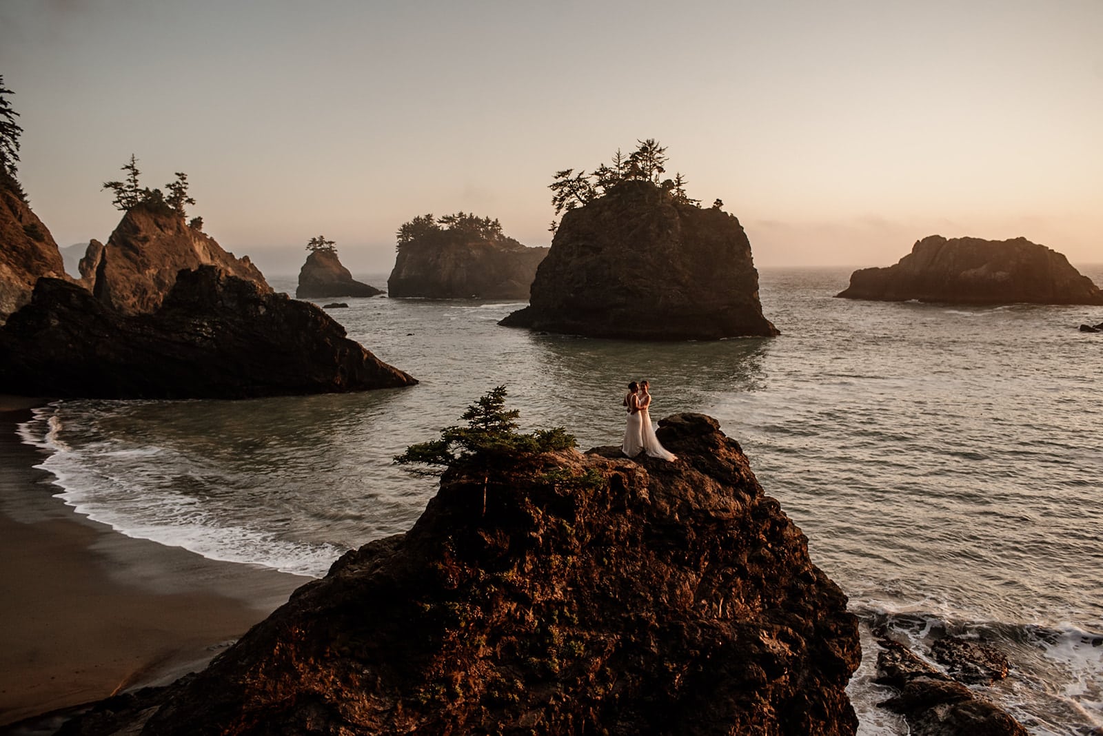 a bride and groom standing on the rocks at sunset