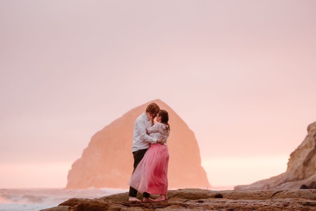a man and woman standing on rocks near the ocean