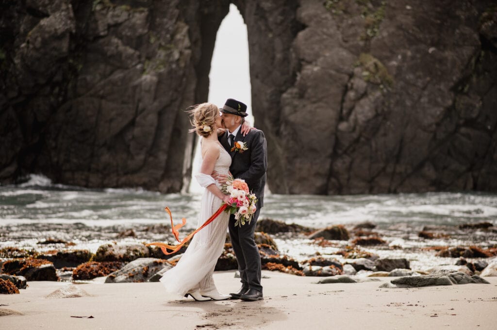 a bride and groom are standing on the beach
