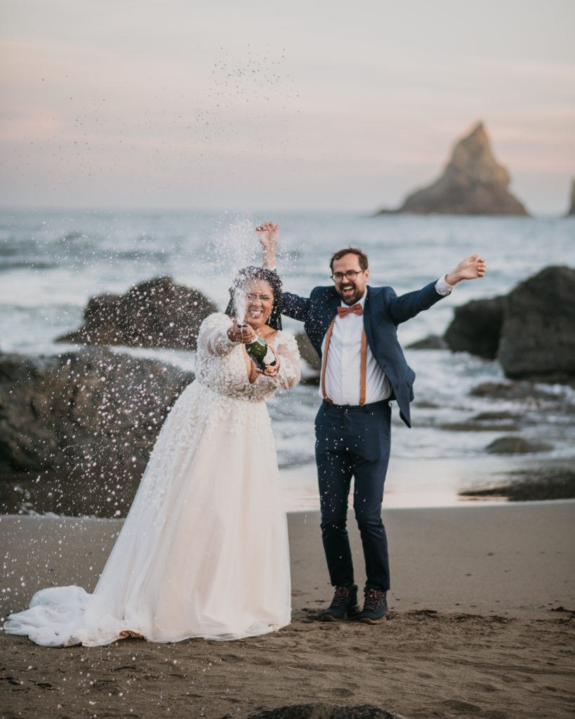 A couple celebrates eloping on the Oregon coast by popping a bottle of champagne