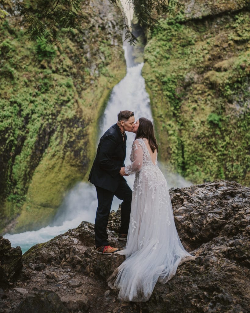 a bride and groom kissing in front of a waterfall