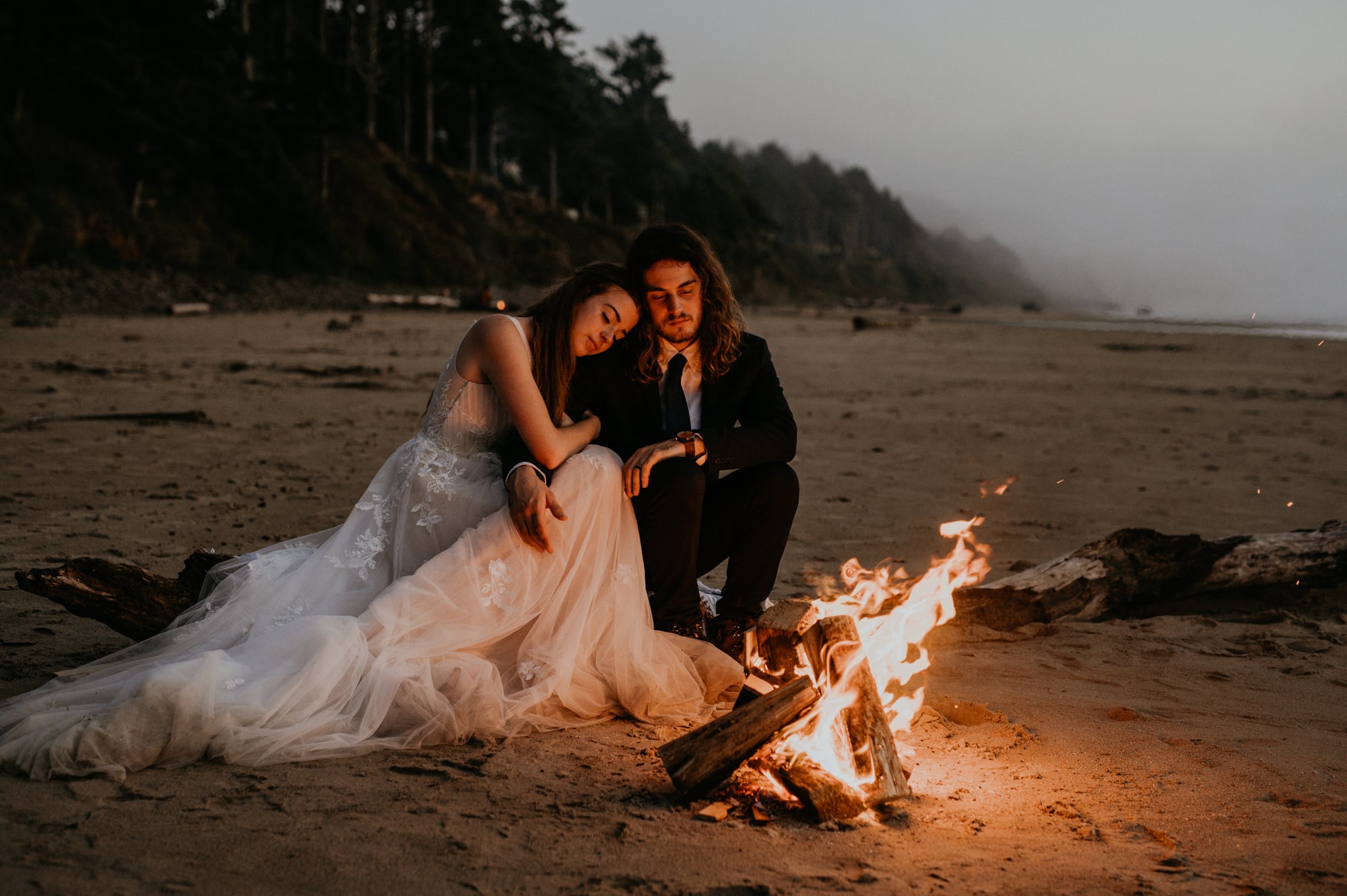 a man and woman sitting next to a fire