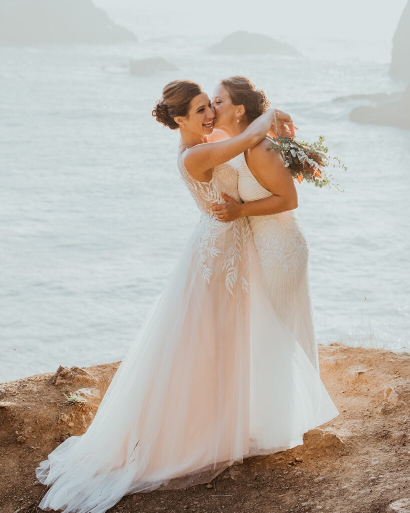 two brides hugging each other on the beach