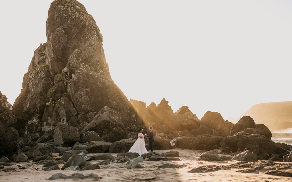 a bride and groom standing on rocks at the beach