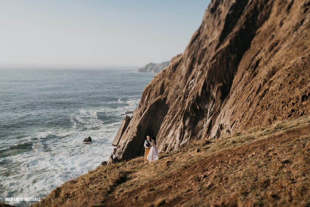 two people standing on a cliff near the ocean
