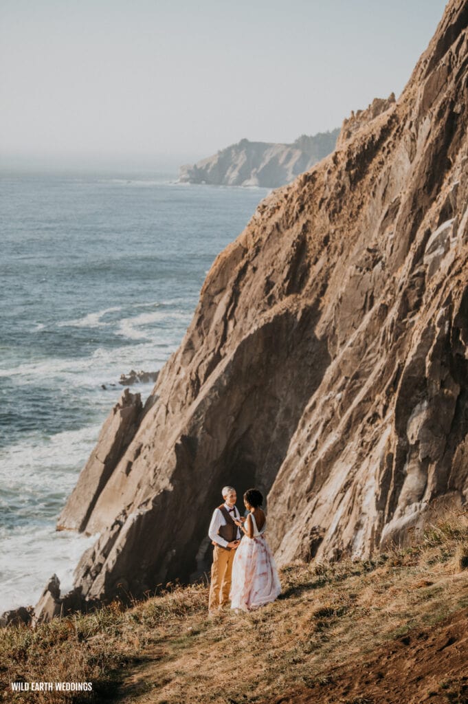 a man and woman are standing on the cliff by the ocean