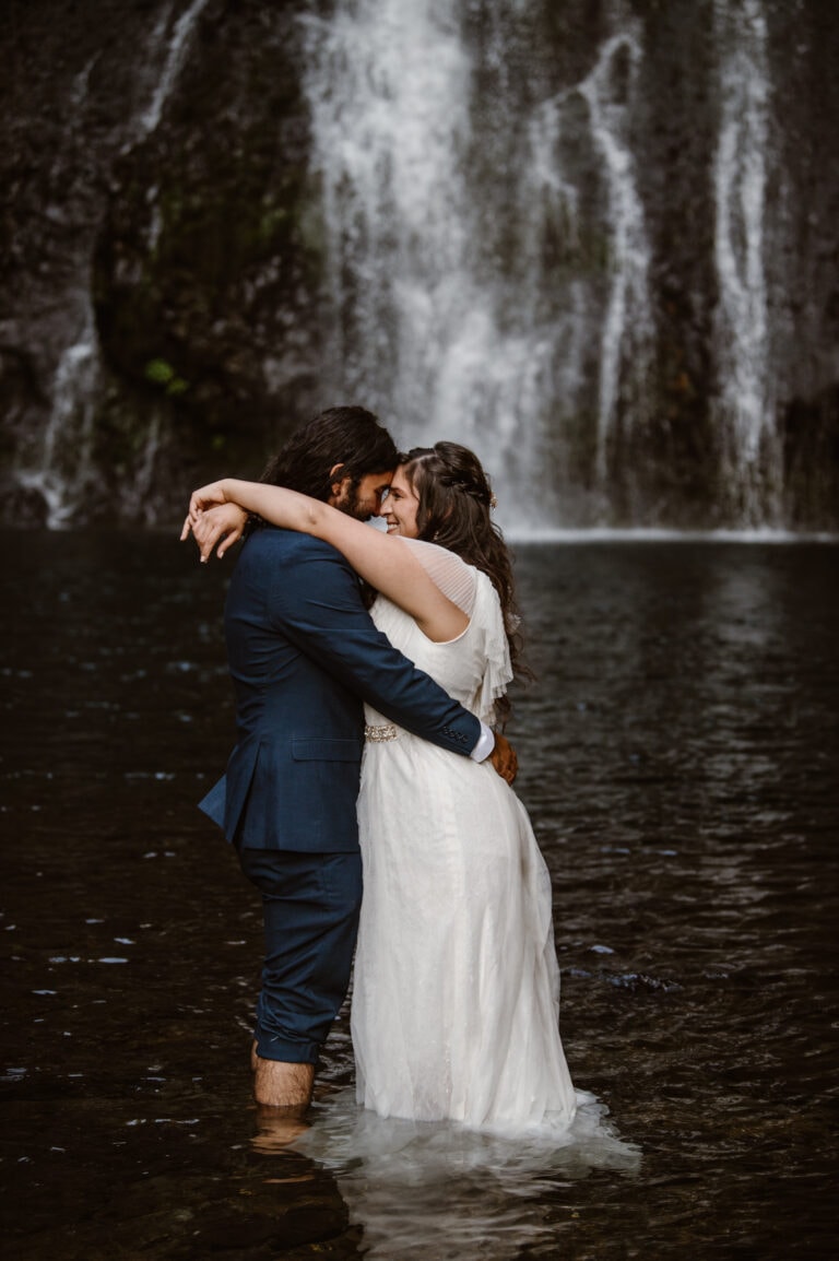 a bride and groom hugging in front of a waterfall