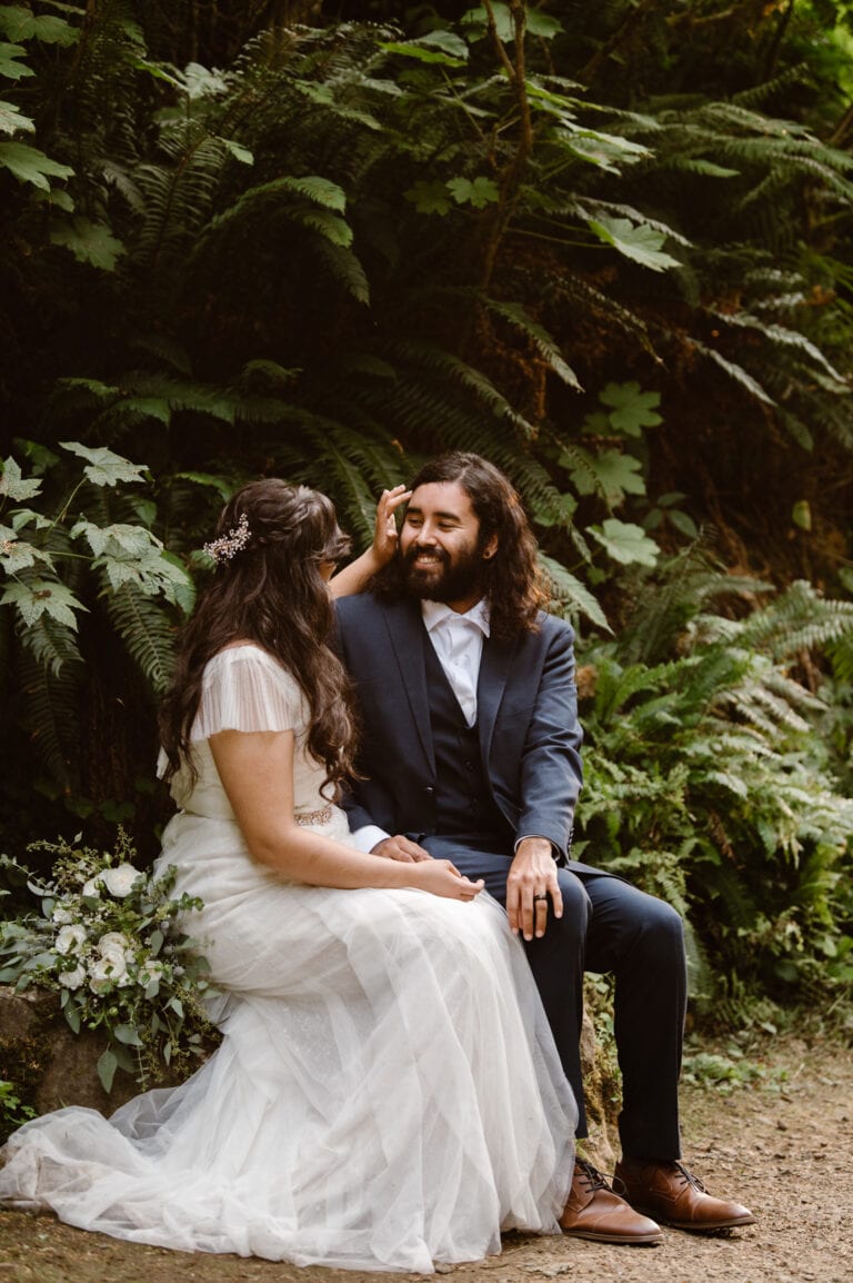 a bride and groom sitting on a bench in the woods