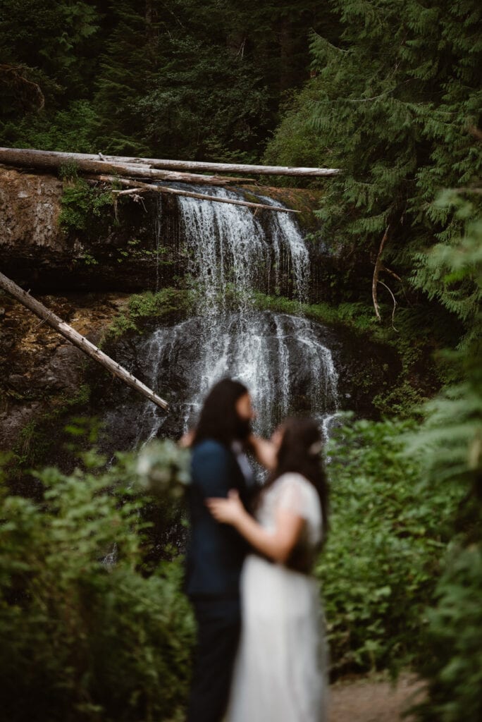 a bride and groom standing in front of a waterfall