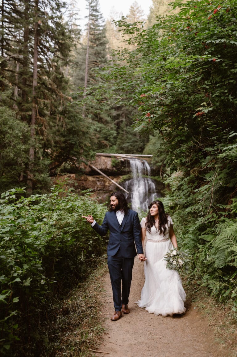 a bride and groom walking down a path in front of a waterfall