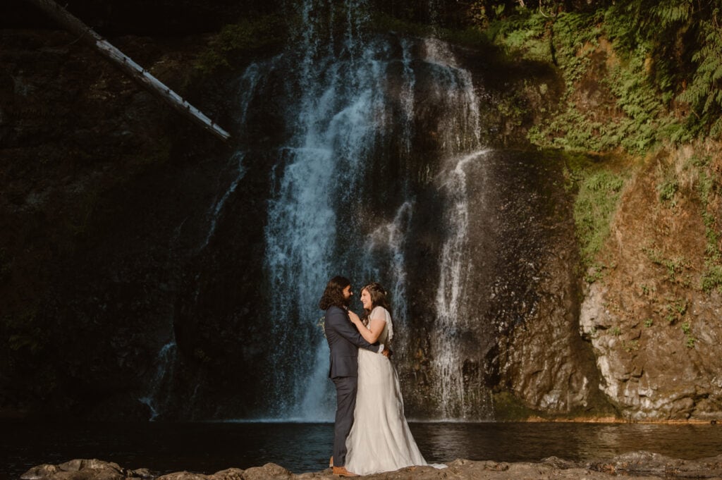 a bride and groom standing in front of a waterfall