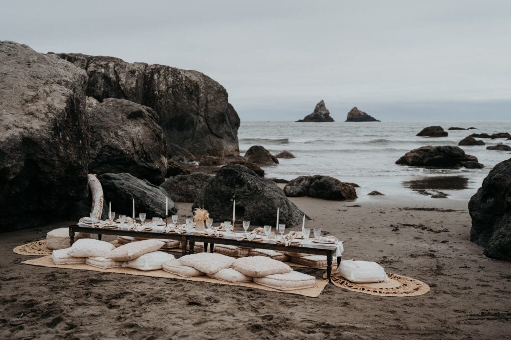 a table set up on the beach with pillows and candles