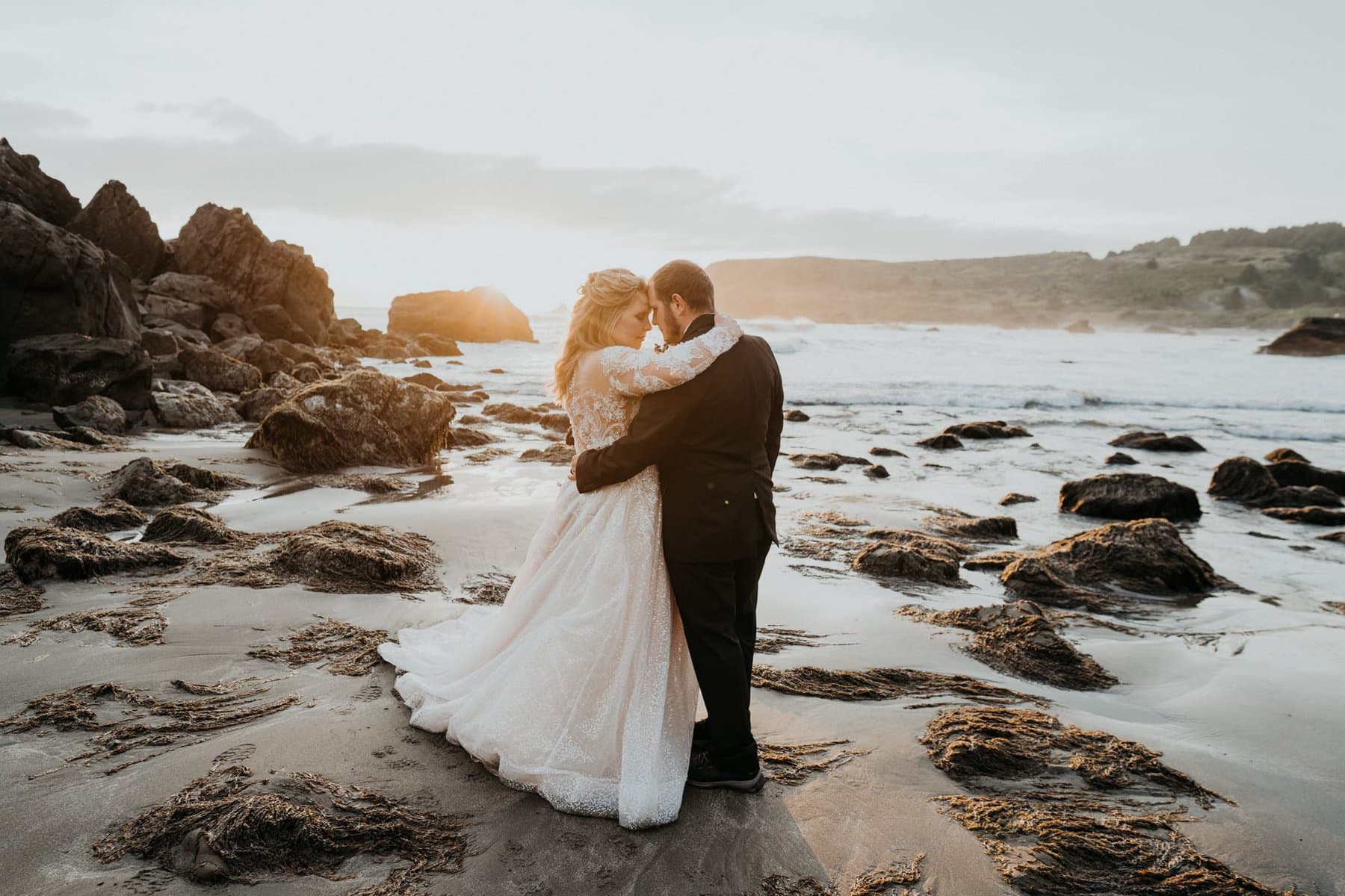 a bride and groom embracing on the beach
