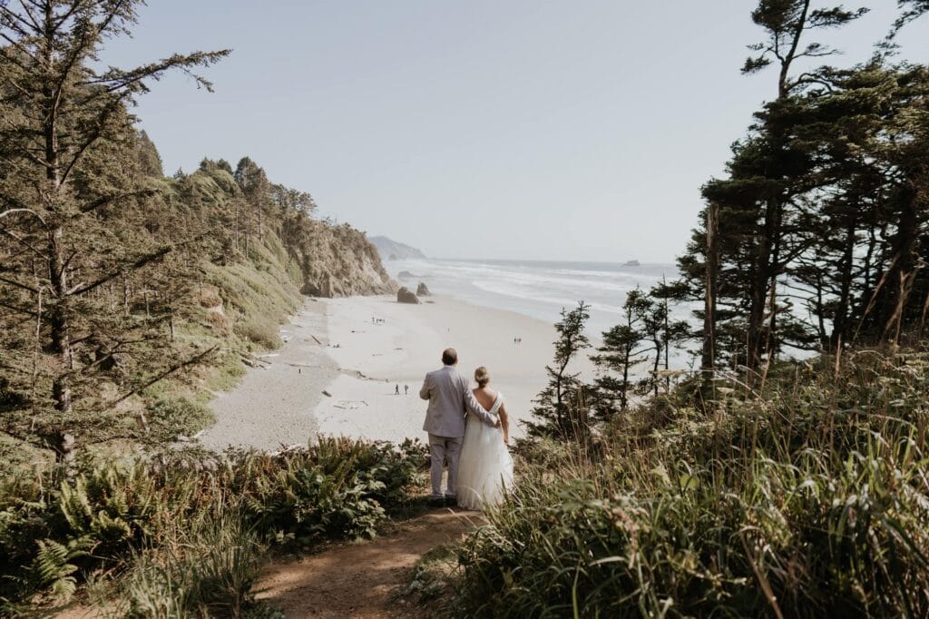 a bride and groom walking down a path to the beach