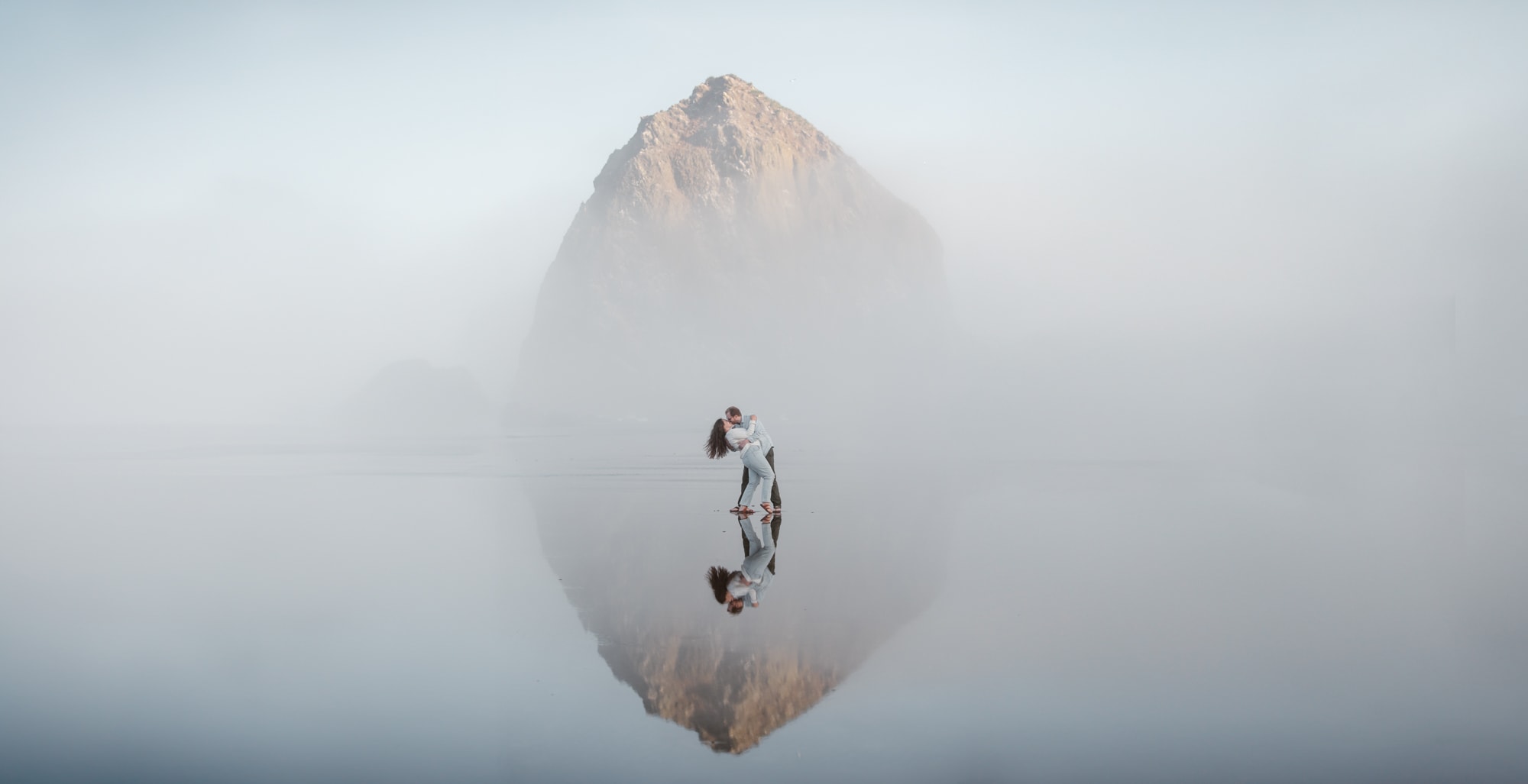 two people standing in front of Haystack Rock on a foggy morning at Cannon Beach.