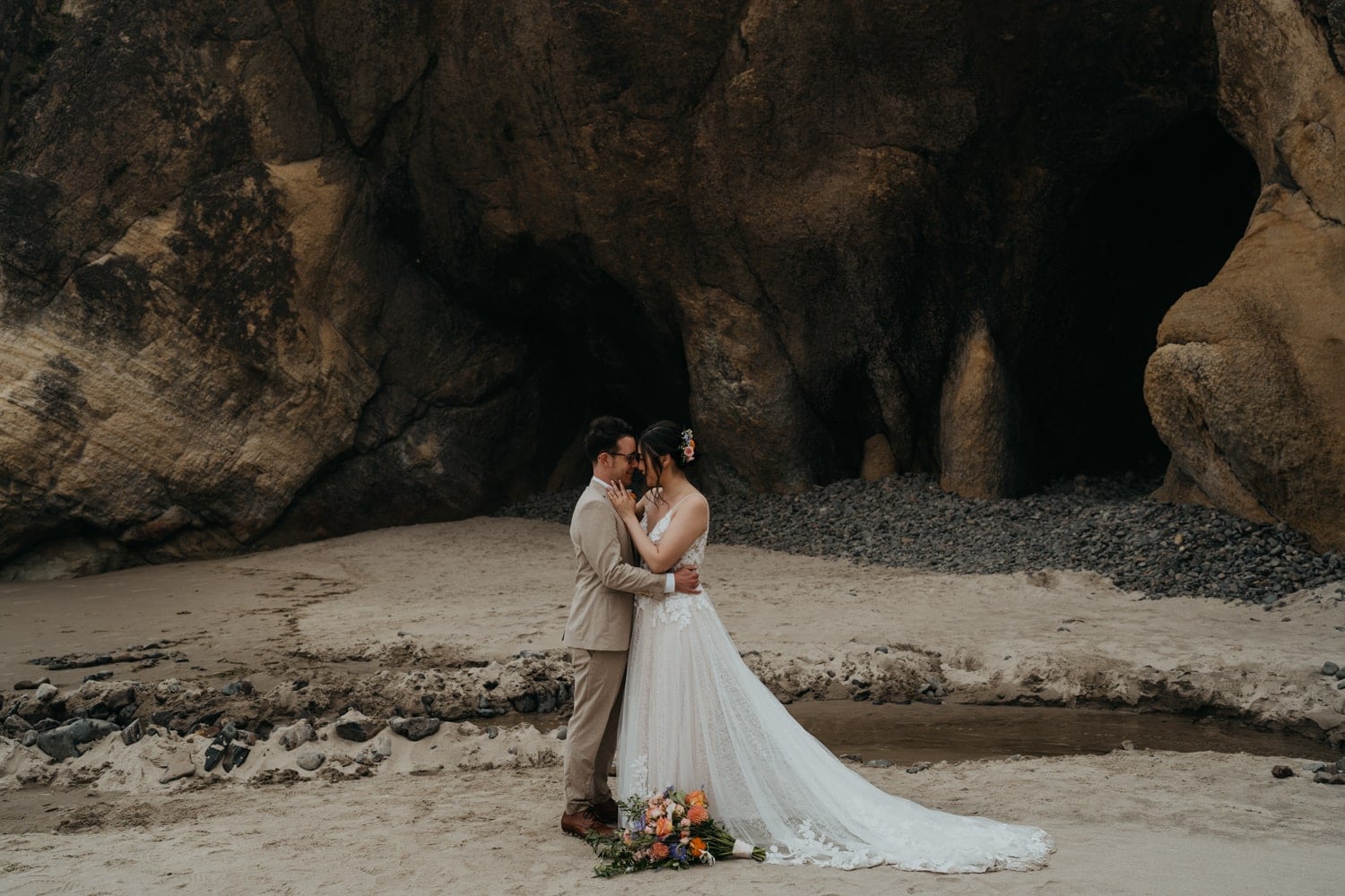 a bride and groom standing in front of a cave at hug point near cannon beach