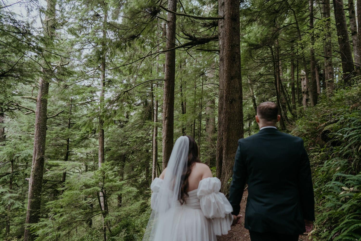 a bride and groom walking through the woods