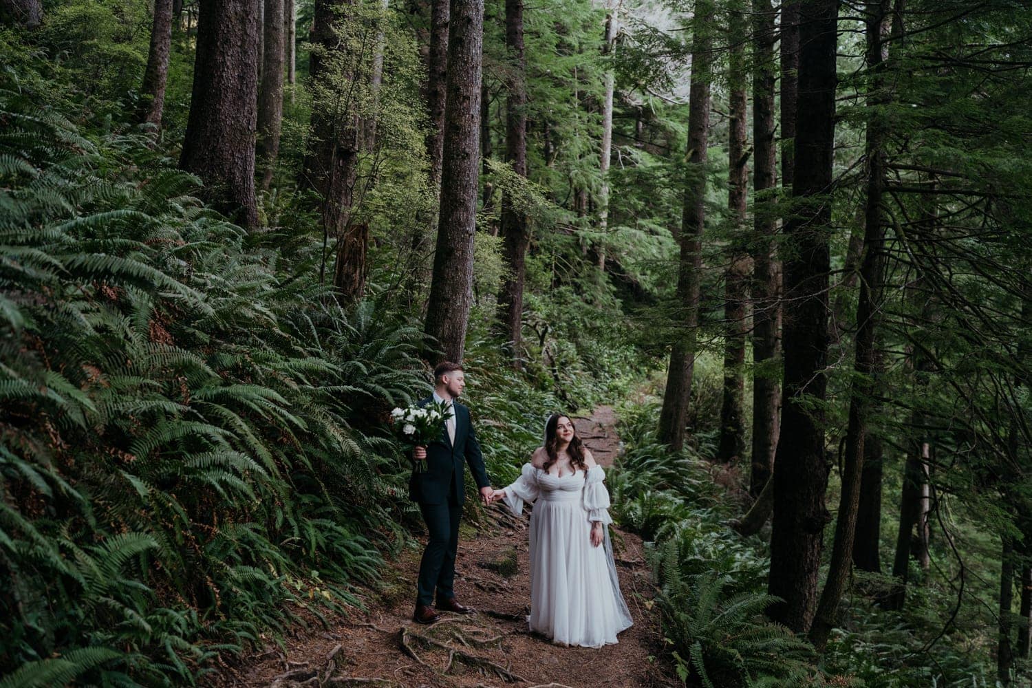 bride and groom take a walk in the forest on the oregon coast