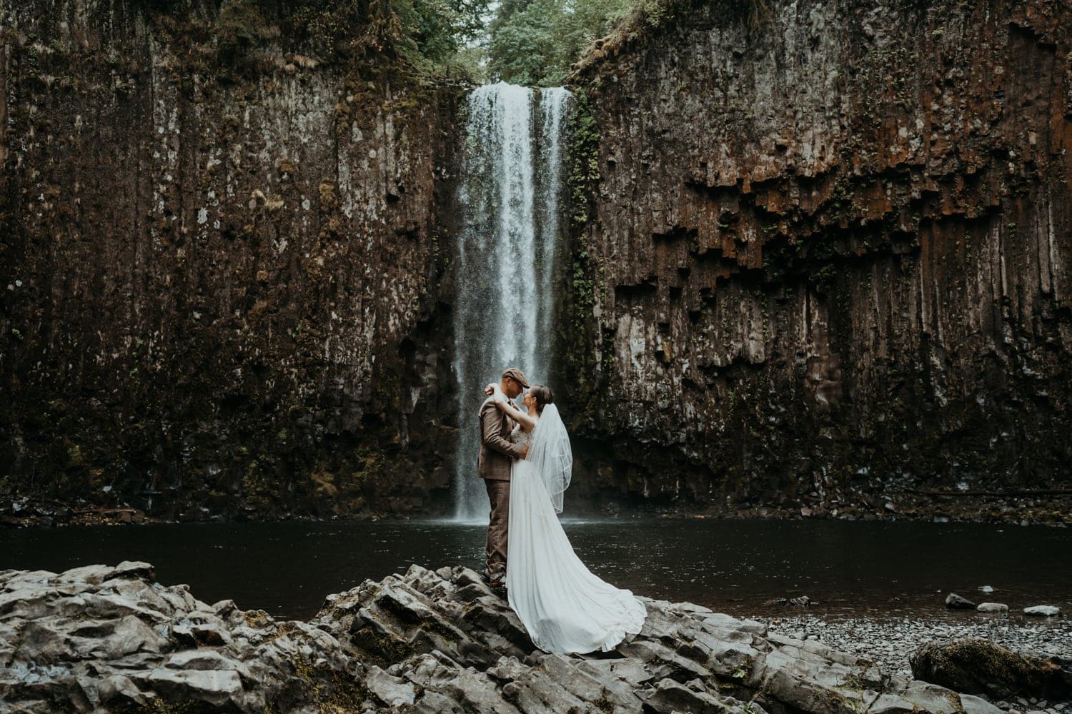 A bride and groom embrace in front of Abiqua Falls.
