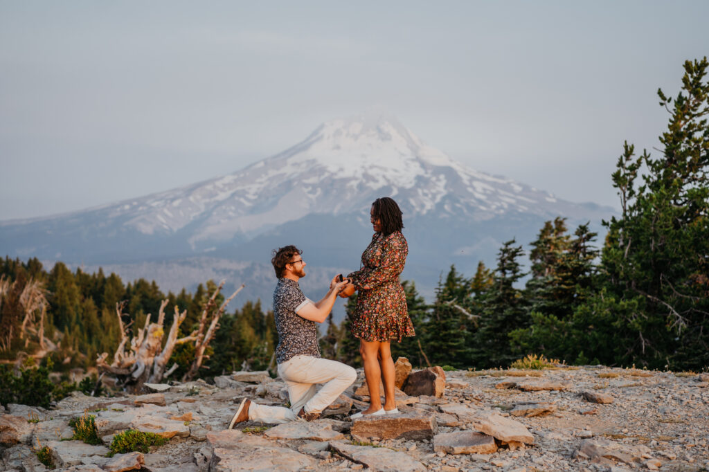 a man kneeling down next to a woman on top of a mountain